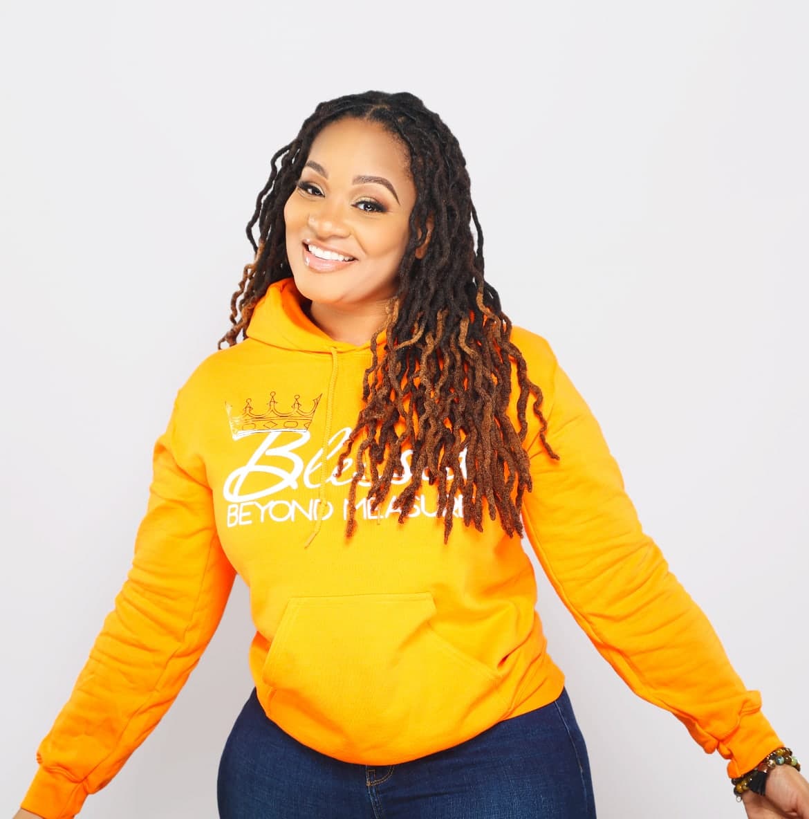 T’Aura the Poet smiling in an orange Blessed Beyond Measure hoodie